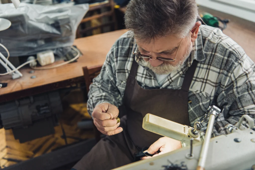 Fabricante de calzado industrial con barba canosa y gafas, concentrado en su taller, examinando un zapato.
