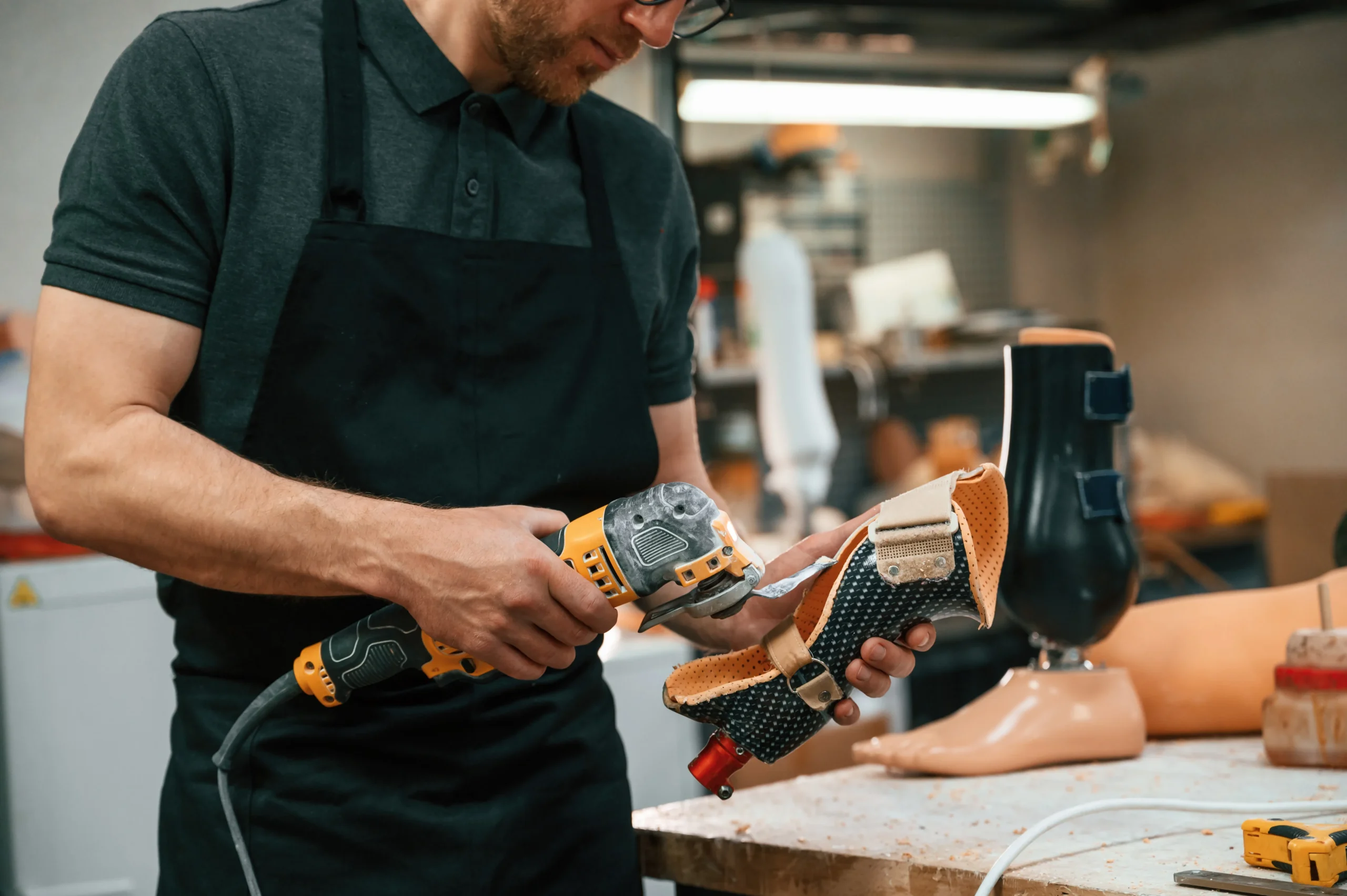 Un joven fabricante de calzado industrial, con barba y gafas, puliendo una pieza de calzado en un entorno de fabricación